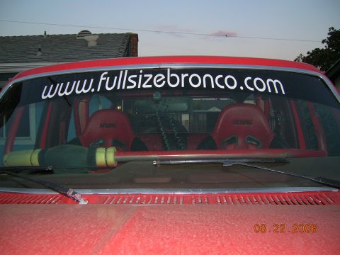 1985 Ford Bronco - The photo shows the interior of a vehicle with racing seats and a website banner on the windshield.