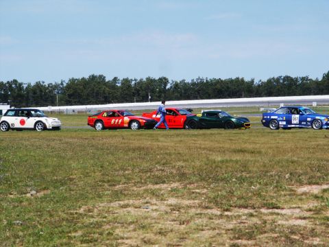 2001 Mercury Grand Marquis - Multiple vehicles are parked on a grassy area next to a race track under a clear blue sky.