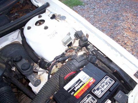 1990 Dodge Shadow - View of a car's engine bay, showing the battery, various electrical components, and a set of keys resting on the strut tower.