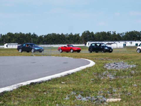 2001 Mercury Grand Marquis - Multiple vehicles are visible on a paved track under a clear blue sky, with a line of trees and buildings in the distance.