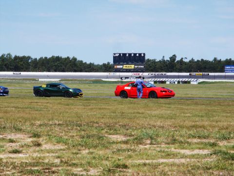 2001 Mercury Grand Marquis - A red sports car is parked on the grass next to a race track with a scoreboard in the background.