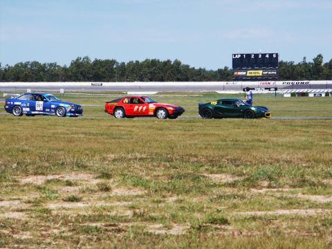 2001 Mercury Grand Marquis - Three race cars are lined up on a grassy track with a scoreboard in the background.