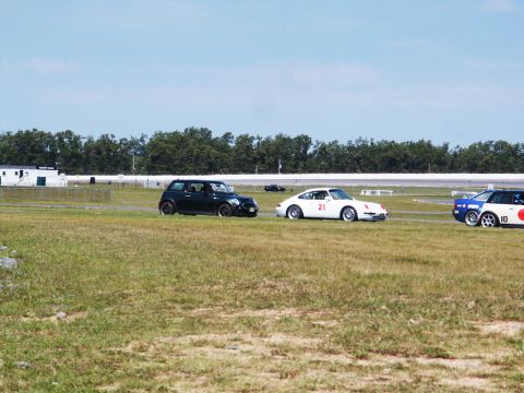 2001 Mercury Grand Marquis - Multiple vehicles compete on a sunny day at a race track, with a black Mini Cooper, a white Porsche 911 with number 21, and a blue and whit…