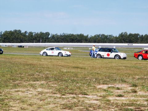 2001 Mercury Grand Marquis - Several cars are on a grassy area next to a racetrack under a clear sky.