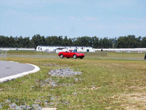 2001 Mercury Grand Marquis - A red convertible sports car drives on a racetrack with buildings and trees in the background.