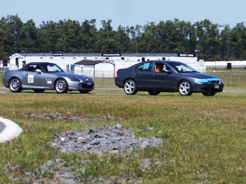 2001 Mercury Grand Marquis - Two cars are on a race track, one is a silver convertible and the other is a dark sedan.