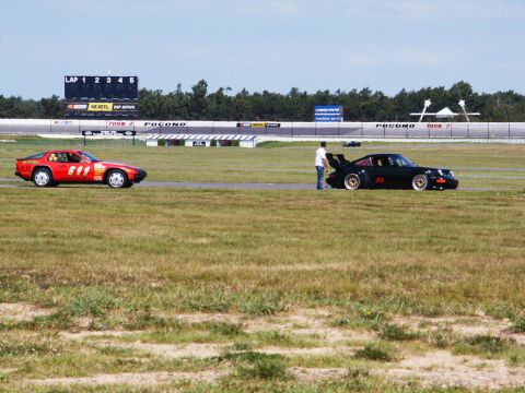 2001 Mercury Grand Marquis - Two sports cars are on a racetrack with a scoreboard and trees in the background.