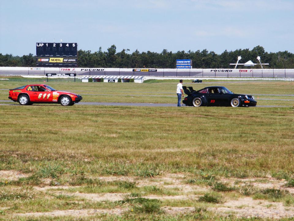 Red sports car with number 611 and black sports car with number 22 on a racetrack with a scoreboard in the background