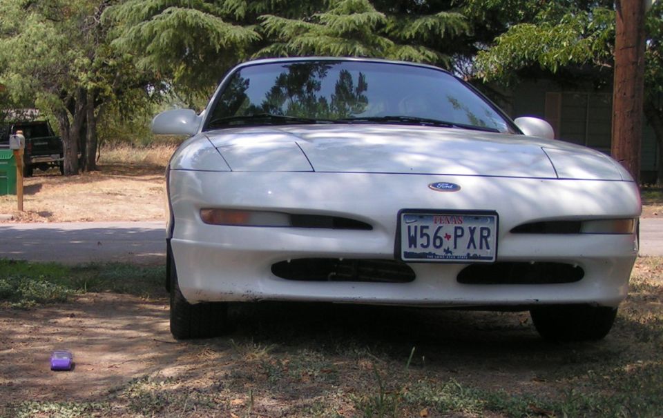Front view of a white Ford coupe with Texas plate W56-PXR parked on dirt