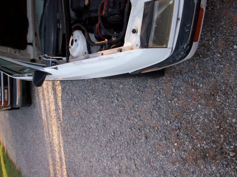 1990 Dodge Shadow - The engine bay and front fender of a white car are visible, with another vehicle partially seen to the left.