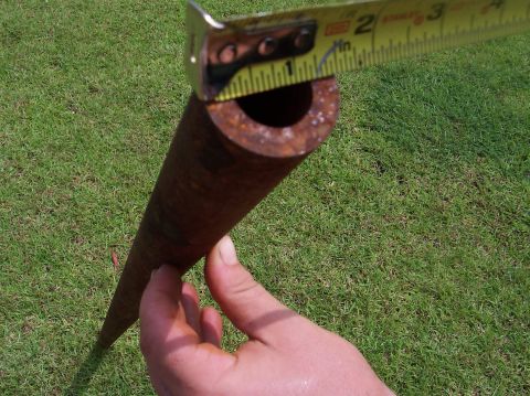 1979 Ford Bronco - A rusty pipe is measured with a tape measure, showing its diameter against a backdrop of green grass.