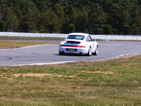 2001 Mercury Grand Marquis - A white Porsche 911 navigates a turn on a race track, with trees and a fence in the background.