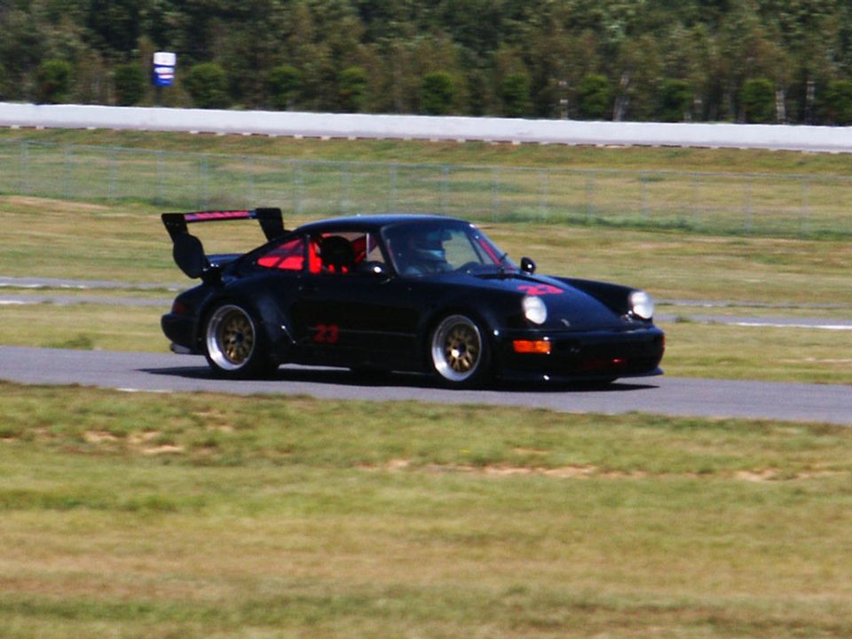 Black Porsche 911 with a large rear spoiler and red interior on a race track. Number 23 is visible on the door and hood