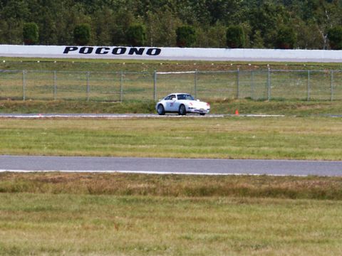 2001 Mercury Grand Marquis - A white Porsche 911 is on the track at Pocono Raceway, with trees and a fence in the background.