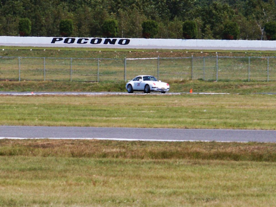 White Porsche 911 on a race track with 'POCONO' sign in background