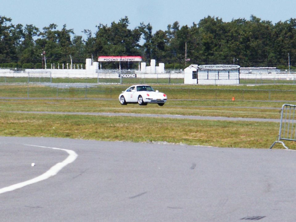White sports car on a race track, front 3/4 view. Pocono Raceway signage in background