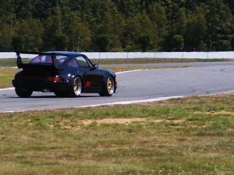2001 Mercury Grand Marquis - A black Porsche 911 race car with a prominent rear spoiler and gold wheels navigates a turn on a sunny day at the racetrack.