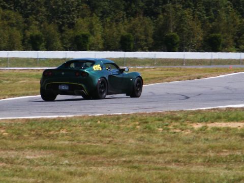 2001 Mercury Grand Marquis - A green sports car navigates a turn on a race track, with trees and a safety fence in the background.