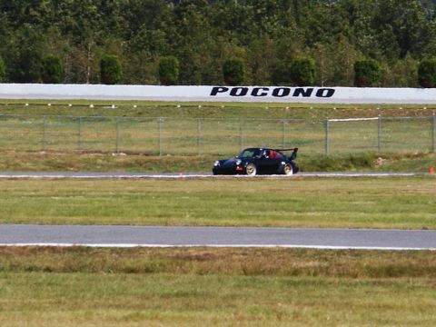 2001 Mercury Grand Marquis - A black sports car races on a track, with 'POCONO' branding on the wall in the background.