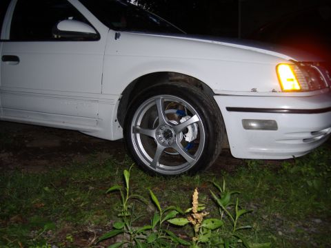 1998 Ford Taurus - The front passenger side of a white sedan is shown, custom wheels and an illuminated turn signal.