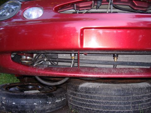1998 Ford Taurus - Front view of a red 1998 Ford Taurus, showing the bumper, grille, and radiator with spare tires supporting the vehicle.