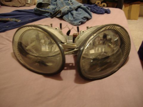 1998 Ford Taurus - A pair of car headlights are shown resting on a surface, with clothing items scattered behind them.