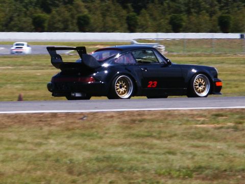 2001 Mercury Grand Marquis - A black Porsche 911 with racing number 23 drives on a track, with another car visible in the distance.