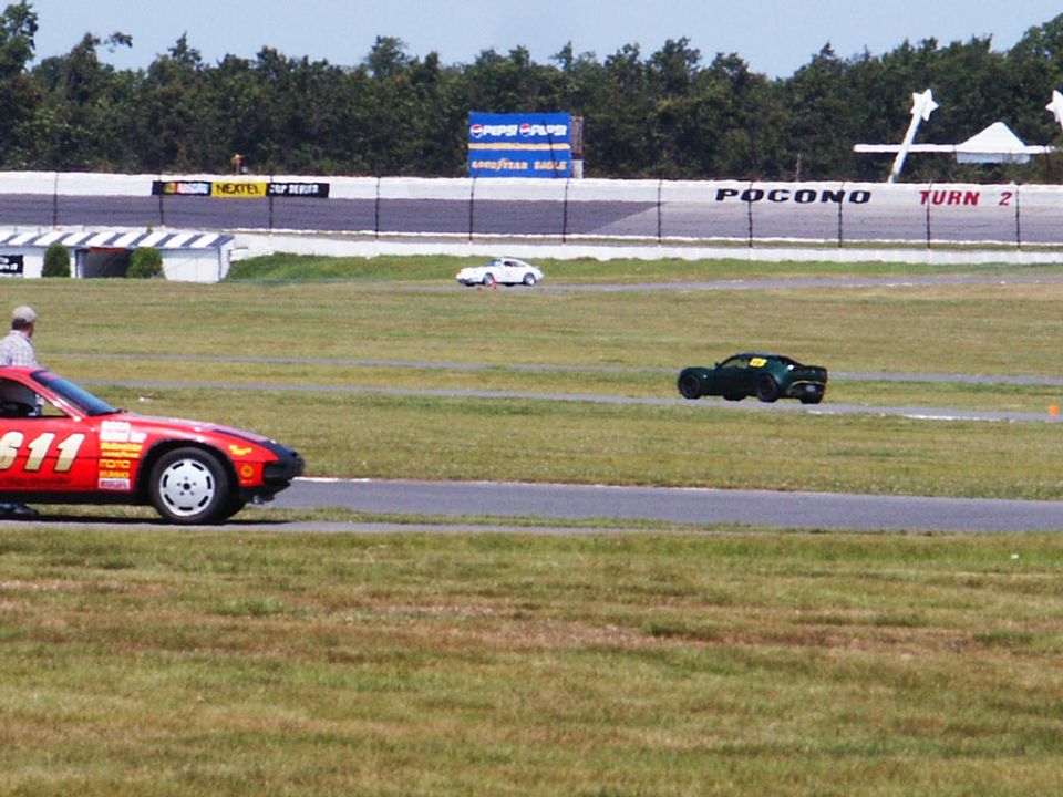 Red race car with number 611 on a track, with other cars and grandstands in the background