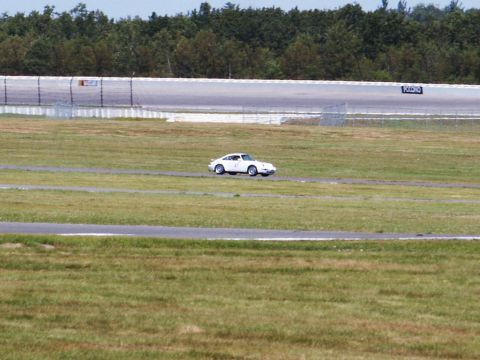 2001 Mercury Grand Marquis - A white sports car is seen on a racetrack with a wooded area and fence in the background.
