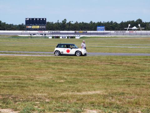 2001 Mercury Grand Marquis - A Mini Cooper is parked on the track at Pocono Raceway, with a scoreboard and grandstands visible in the background.