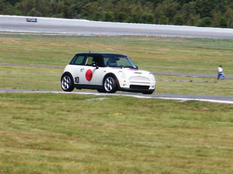 2001 Mercury Grand Marquis - A Mini Cooper with racing decals navigates a turn on a paved race track with grassy infield.