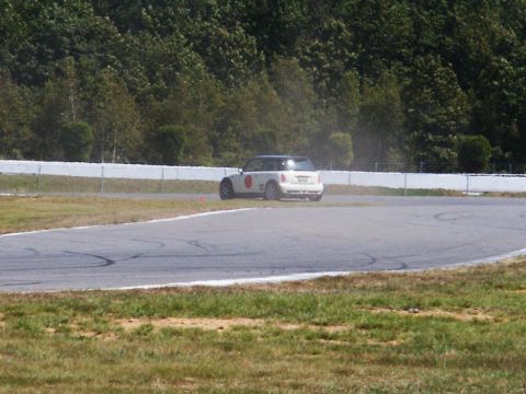2001 Mercury Grand Marquis - A white Mini Cooper navigates a turn on a race track, kicking up a small amount of dust.