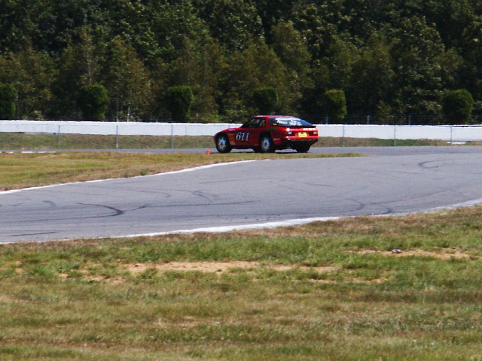 Red sports car with number 611 on the door, on a race track with trees in the background