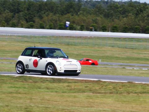 2001 Mercury Grand Marquis - A white Mini Cooper with racing decals is on a track, with another car in the distance. The watermark says Supermotors.net.