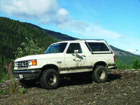 1988 Ford Bronco - A white Ford Bronco is parked on a gravelly surface with a forested mountain in the background.