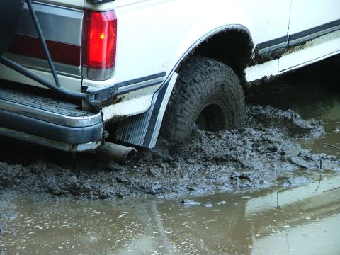 1988 Ford Bronco - This white truck is stuck deep in the mud, with its rear tire submerged.