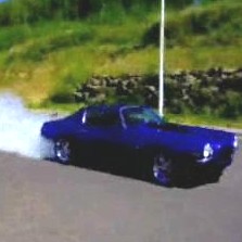 1970 Chevrolet Camaro - 1970 Chevrolet Camaro performing a burnout with smoke from rear tires. SuperMotors.net logo is present.