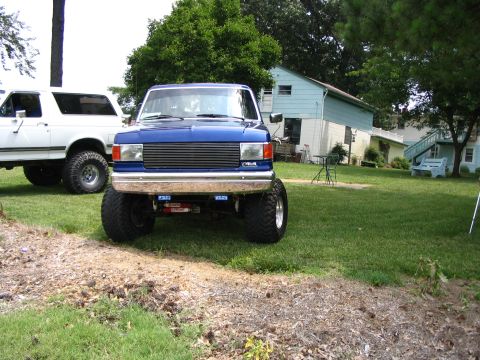 1989 Ford Bronco - A lifted blue 1989 Ford Bronco is parked in a yard next to a white SUV.