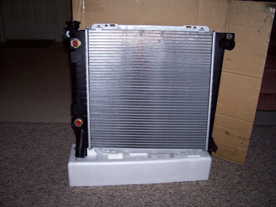 New aluminum radiator with black plastic tanks on foam packing block in front of its shipping box