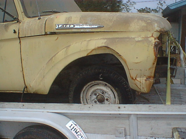 Yellow vintage pickup front fender with F-100 emblem and steel wheel, on a trailer