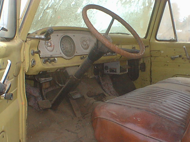 Dusty interior of old pickup with worn steering wheel, oval gauge cluster, orange bench seat