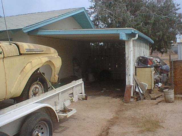 Yellow pickup front clip on trailer parked beside open wood-frame carport