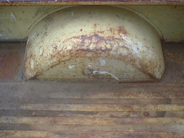 Rusted sheet-metal wheel hump inside pickup bed with peeling yellow paint