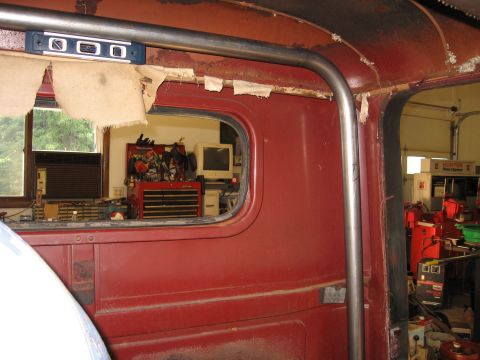 1977 Ford F-150 - Interior view of a red truck cab, showing a roll cage and a glimpse of a workshop through the window.