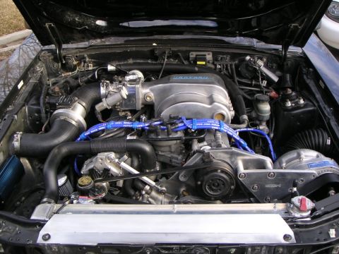 1969 Ford Mustang - The engine bay of a black Ford Mustang, likely from the 1990s, features a Vortech supercharger and blue spark plug wires.