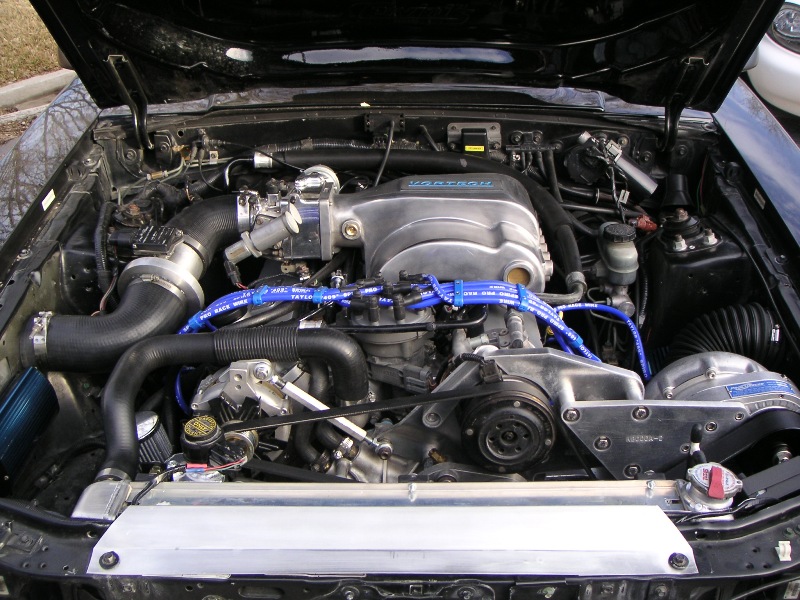 Engine bay of a black 1990s Ford Mustang with a Vortech supercharger