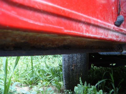 1993 Ford Bronco - Close-up view of the lower body panel and tire of a red vehicle, showing signs of rust.