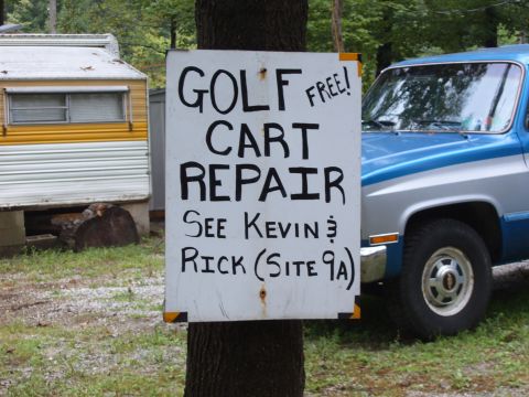 1993 Ford Bronco - A sign for golf cart repair is posted on a tree next to a blue and silver pickup truck.
