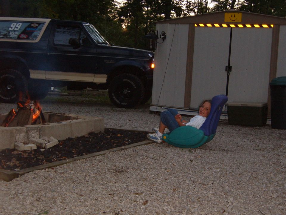 Dark blue 1993 Ford Bronco with racing decal on rear window parked near a fire pit