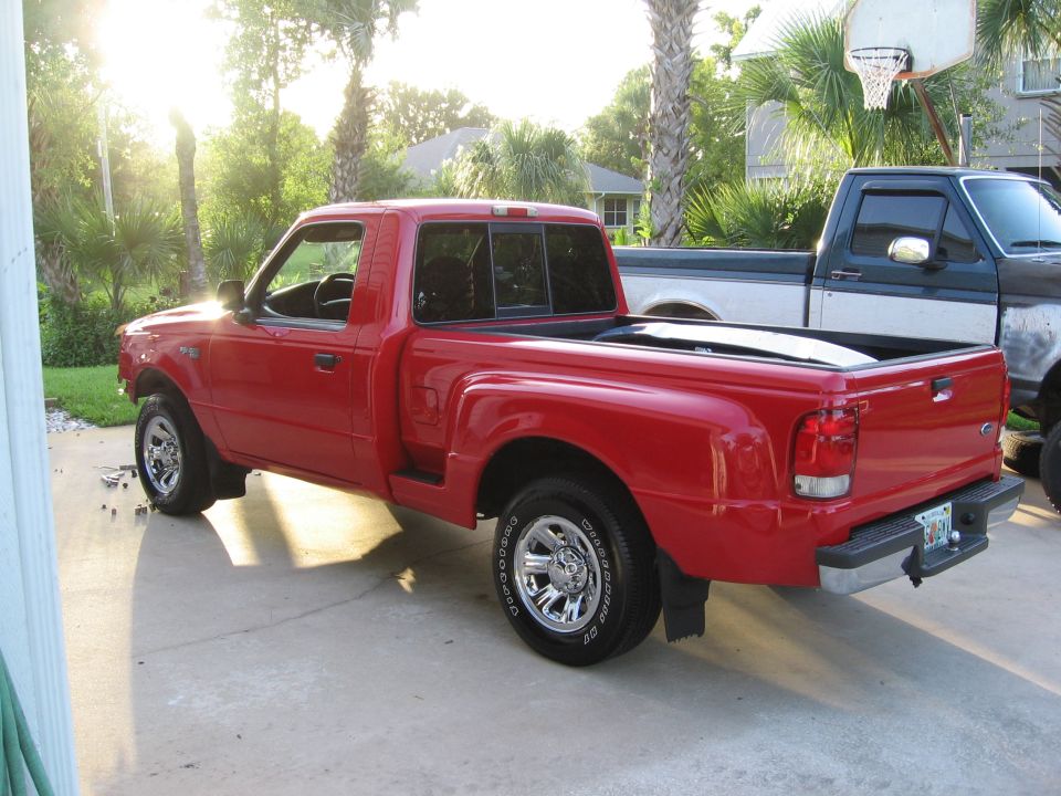 Red Ford Ranger pickup truck parked in driveway next to a dark green and silver Ford pickup